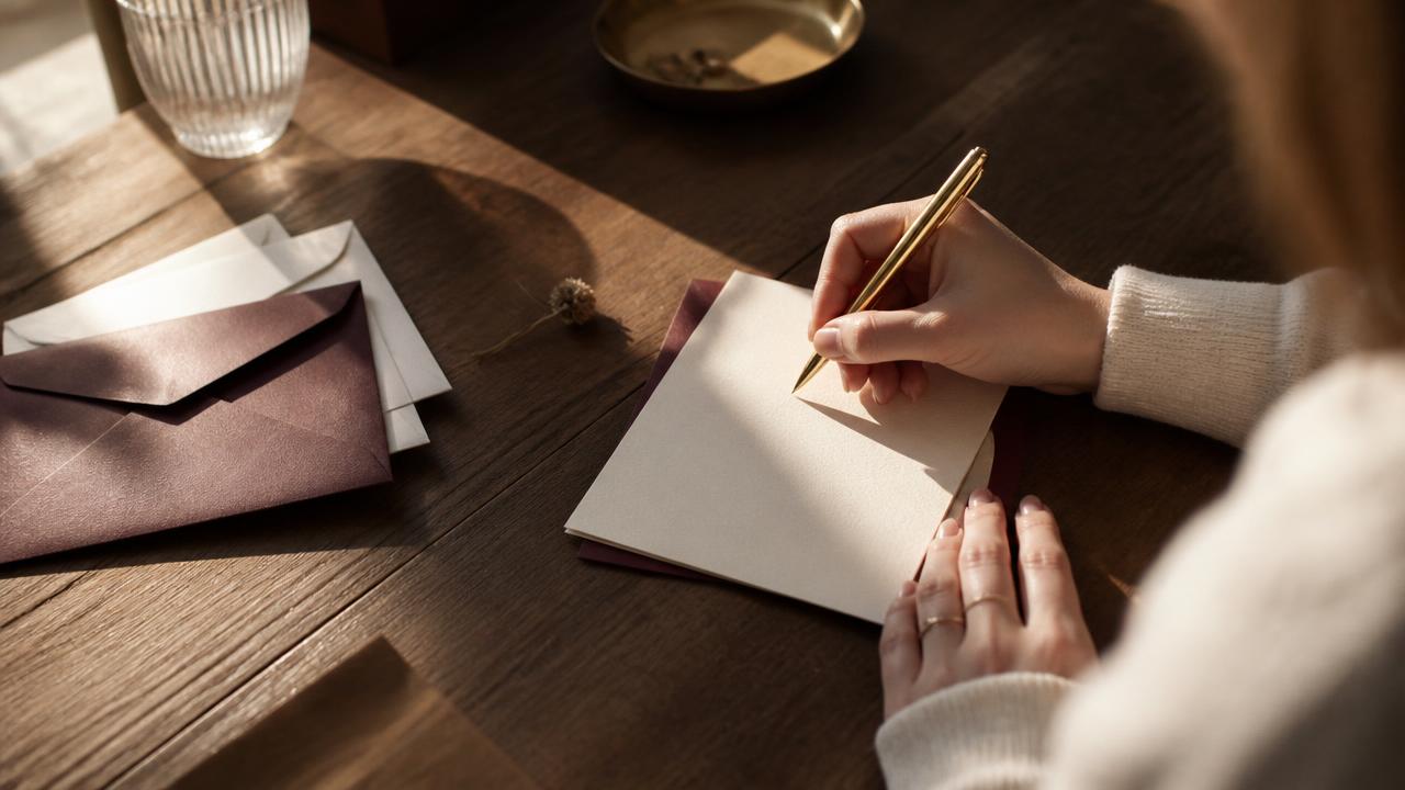 Hand writing a thank-you card on a wooden desk with warm sunlight